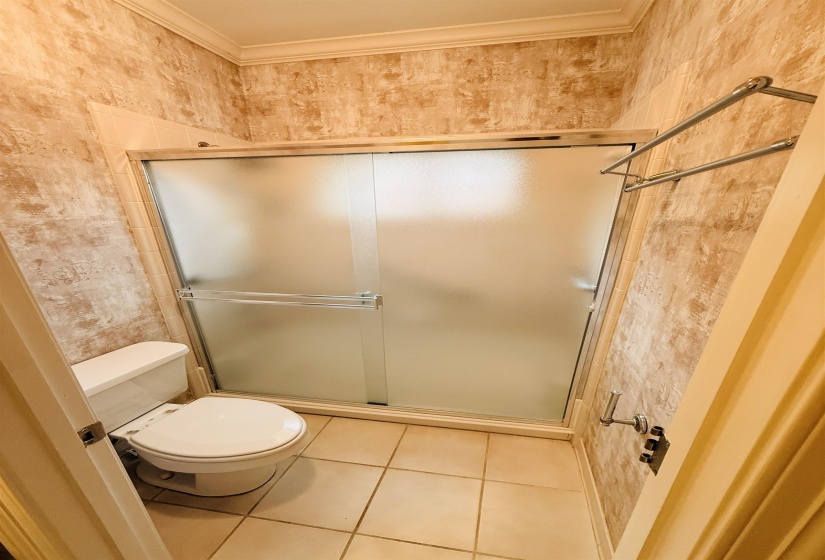 Bathroom with ornamental molding, a stall shower, light tile patterned floors, and wallpapered walls