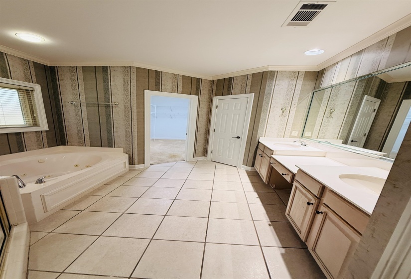 Full bathroom with a whirlpool tub, double vanity, light tile patterned floors, a stall shower, and ornamental molding