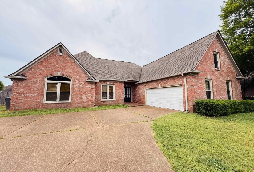 Traditional home with roof with shingles, brick siding, driveway, an attached garage, and a front lawn