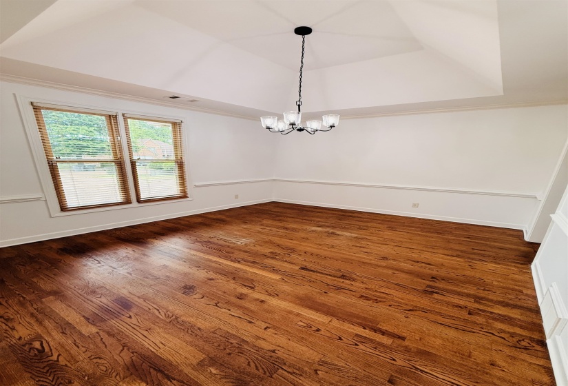 Unfurnished dining area with a tray ceiling, suspended lighting, crown molding, and dark wood-type flooring