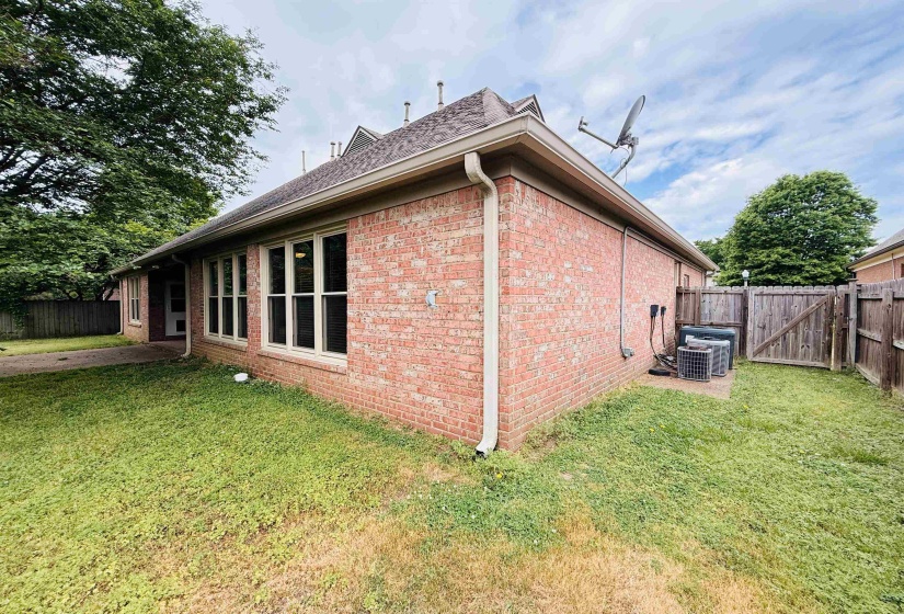 View of side of property featuring a fenced backyard, brick siding, and a gate