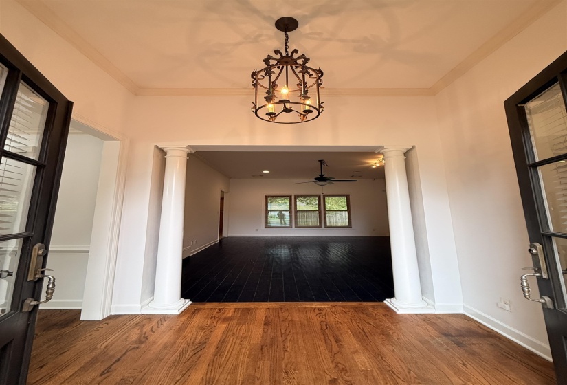 Entrance foyer featuring crown molding, dark wood finished floors, decorative columns, and hanging lights