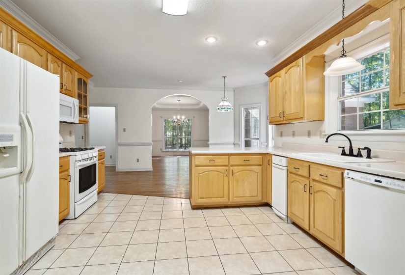 Kitchen with white appliances, light countertops, a peninsula, arched walkways, and ornamental molding