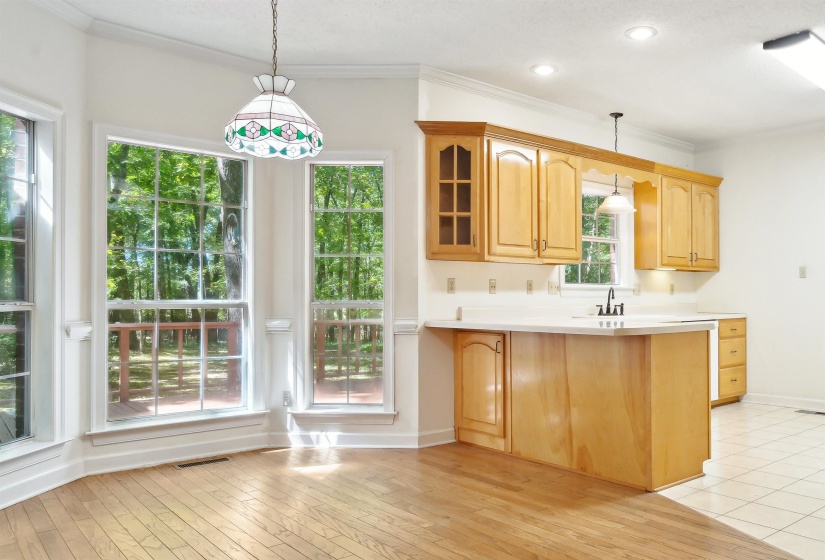 Kitchen featuring light countertops, decorative light fixtures, ornamental molding, glass fronted cabinets, and light wood-style flooring