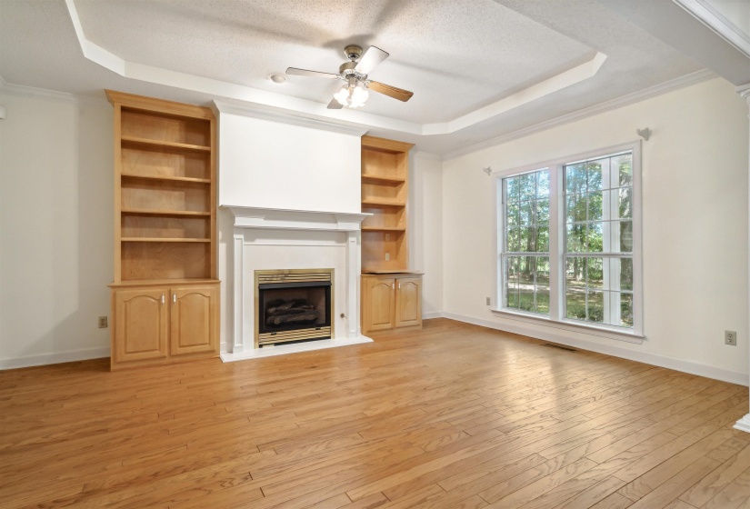 Unfurnished living room with ceiling fan, light wood finished floors, a raised ceiling, crown molding, and a fireplace