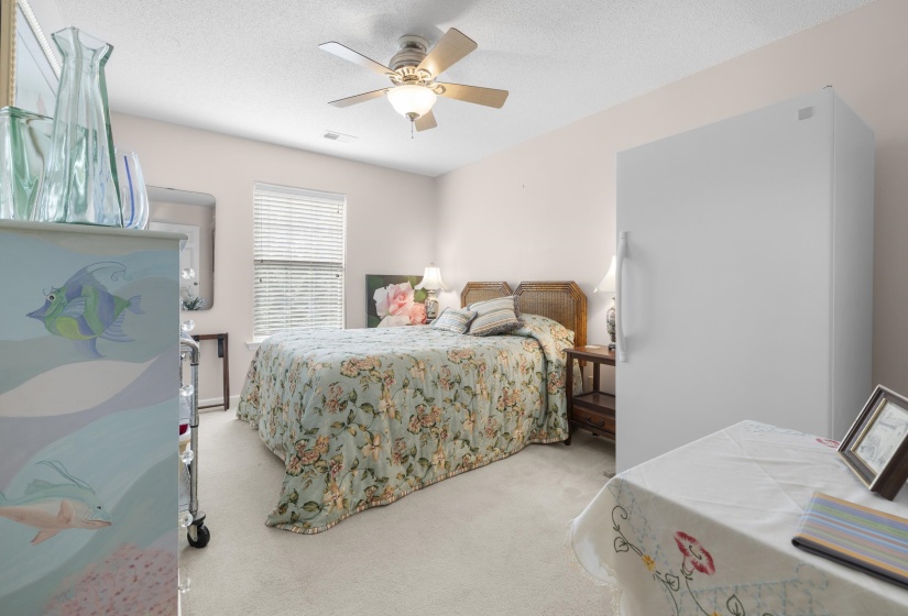 Bedroom with light carpet, ceiling fan, freestanding refrigerator, and a textured ceiling