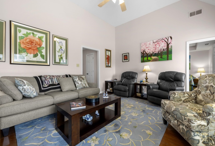 Living area with a ceiling fan, wood finished floors, and a high ceiling