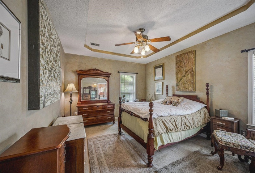 Bedroom featuring a tray ceiling, a textured ceiling, a ceiling fan, and a textured wall