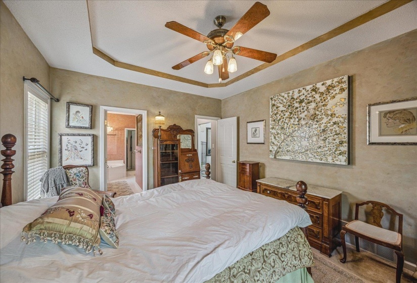 Bedroom with a raised ceiling, a ceiling fan, ensuite bathroom, and a textured wall