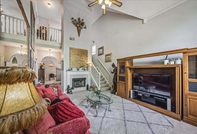 Living room featuring a tile fireplace, ceiling fan, a chandelier, carpet flooring, and vaulted ceiling