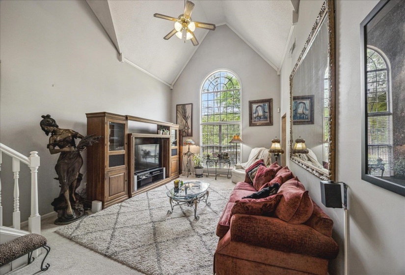 Living room featuring ceiling fan, light carpet, and a high ceiling