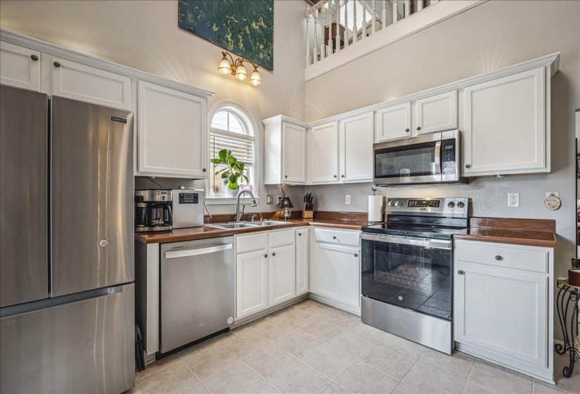 Kitchen featuring stainless steel appliances, white cabinetry, a high ceiling, and light tile patterned flooring