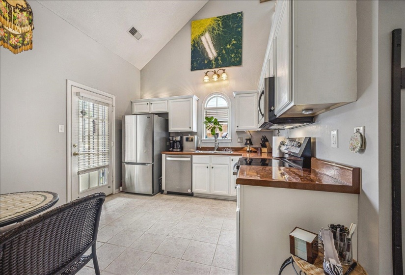 Kitchen featuring white cabinetry, vaulted ceiling, stainless steel appliances, and light tile patterned floors