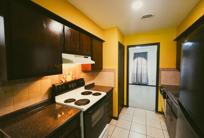 Kitchen with electric stove, dark countertops, freestanding refrigerator, light tile patterned floors, and dark wood finish cabinetry