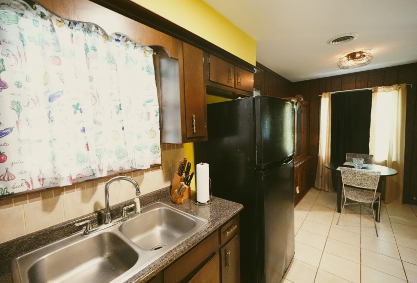 Kitchen featuring freestanding refrigerator, dark countertops, light tile patterned floors, and dark wood finish cabinets