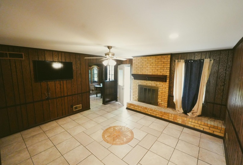 Unfurnished living room featuring wooden walls, a fireplace, a ceiling fan, and light tile patterned floors