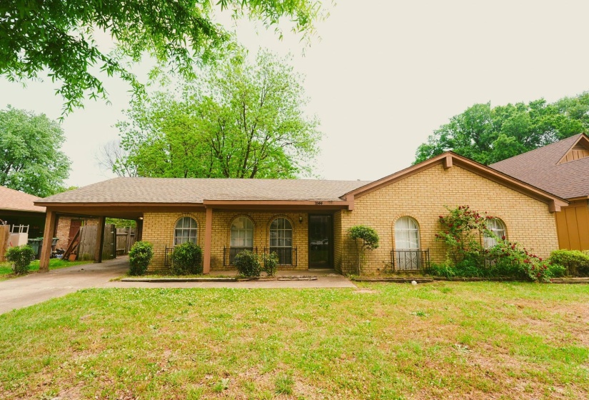 Ranch-style house with a porch, brick siding, an attached carport, and a front lawn