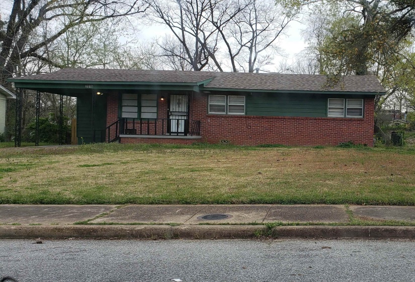 Ranch-style home with a front lawn, covered porch, brick siding, an attached carport, and roof with shingles