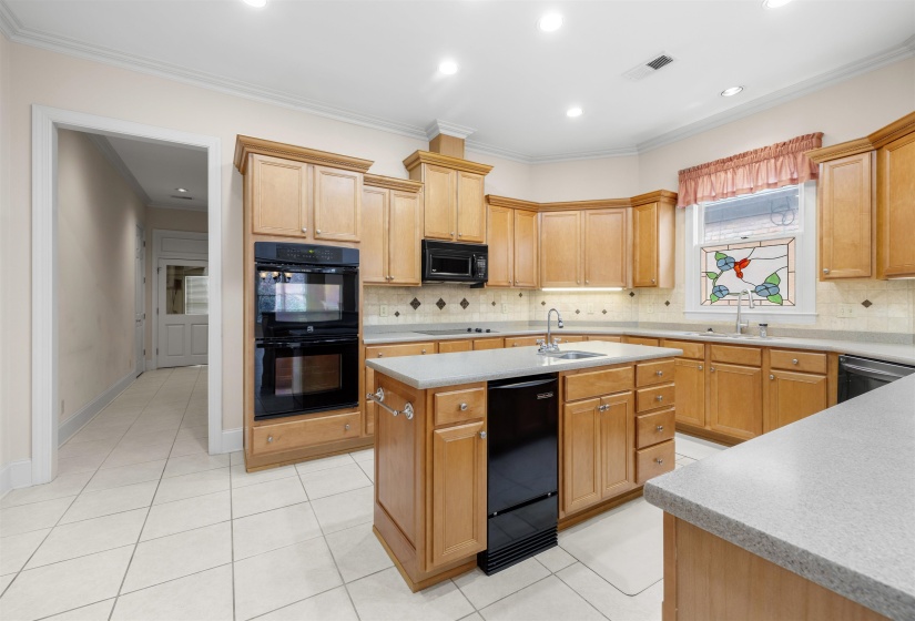 Kitchen featuring black appliances, an island with sink, light tile patterned floors, decorative backsplash, and ornamental molding