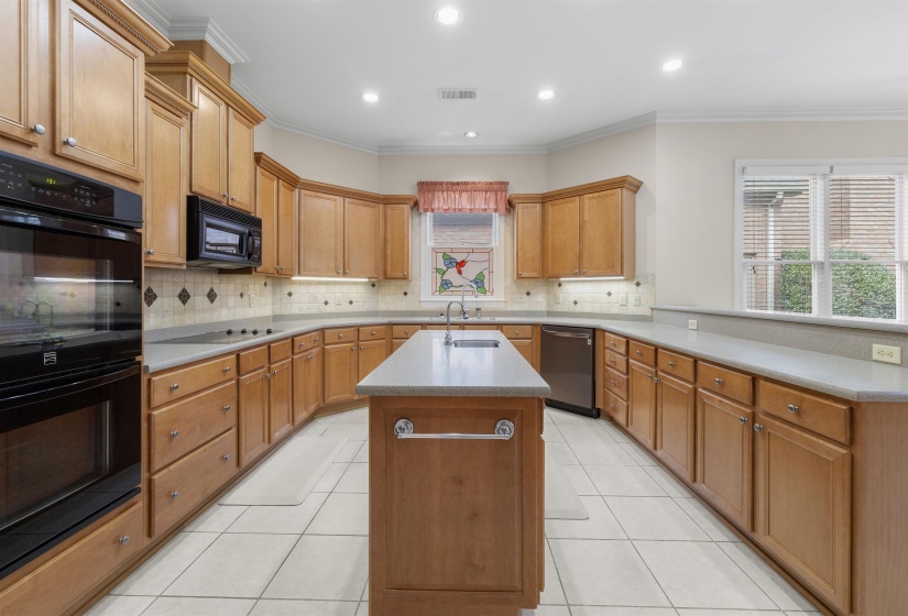Kitchen with black appliances, an island with sink, a peninsula, crown molding, and wood finish cabinetry