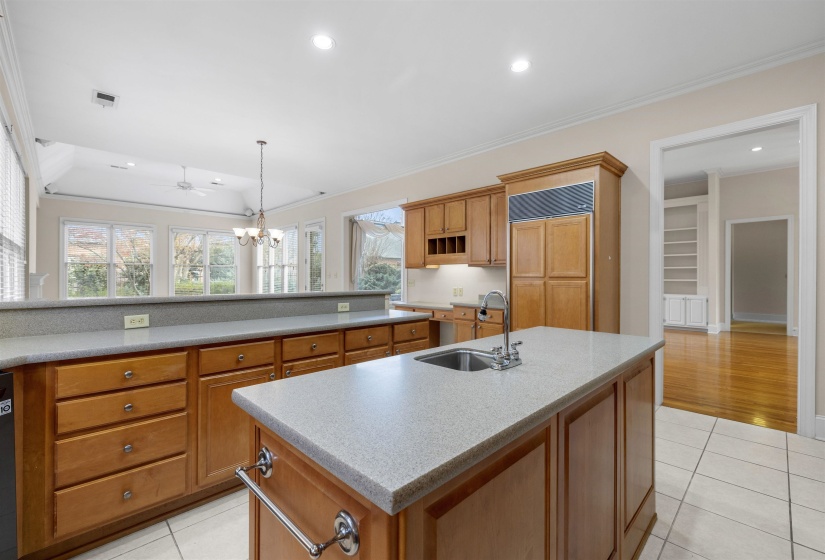Kitchen featuring ornamental molding, a kitchen island with sink, light tile patterned floors, wood finish cabinets, and light stone counters