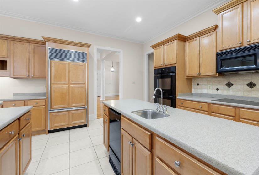 Kitchen with black appliances, ornamental molding, light tile patterned floors, light stone counters, and decorative backsplash
