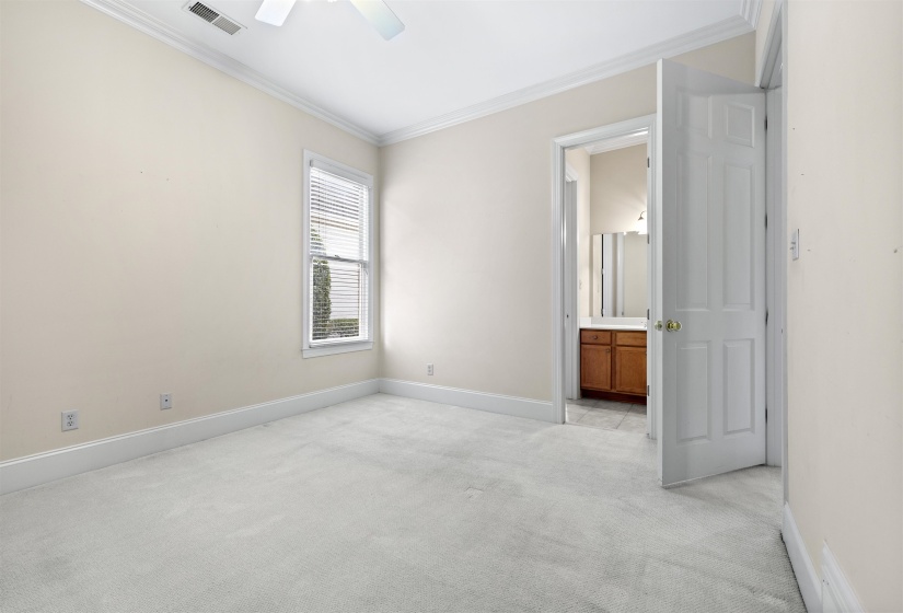 Unfurnished bedroom featuring light colored carpet, crown molding, ceiling fan, and ensuite bath