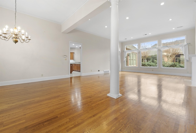 Unfurnished living room featuring hanging lights, light wood finished floors, decorative columns, and ornamental molding