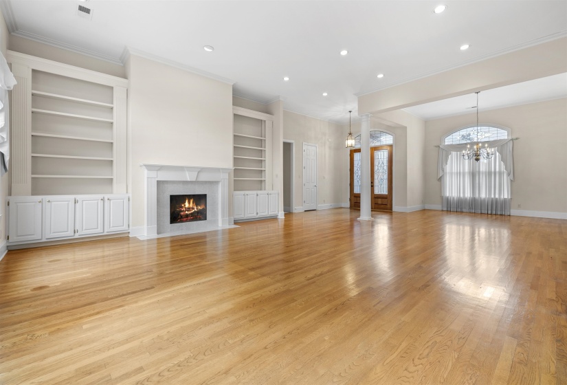 Unfurnished living room with built in features, a high end fireplace, light wood finished floors, crown molding, and a chandelier
