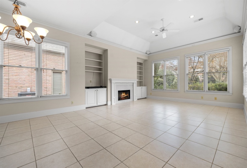 Unfurnished living room with built in shelves, a raised ceiling, a chandelier, a ceiling fan, and light tile patterned floors