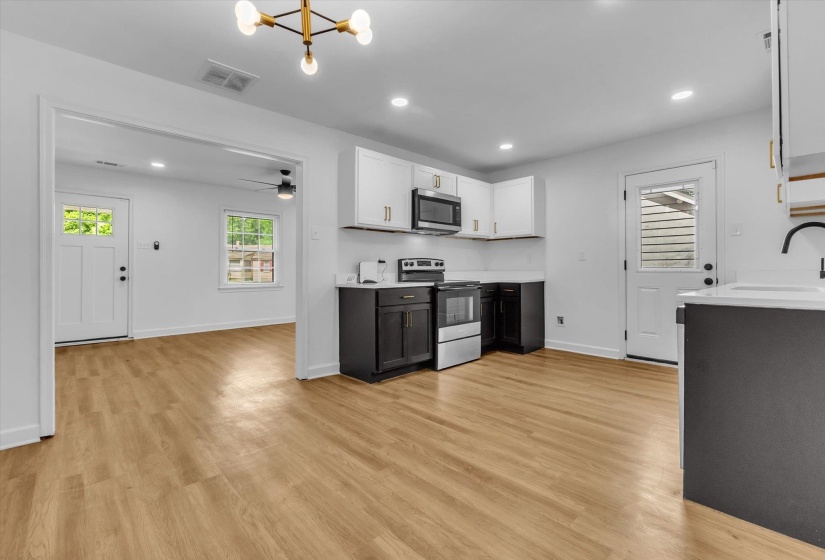 Dual tone kitchen with dual tone cabinets, light countertops, stainless steel appliances, light wood-style flooring, and a chandelier
