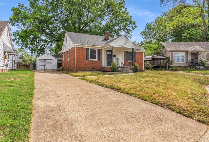View of front of home featuring brick siding, a front yard, concrete driveway, an outdoor structure, and a chimney