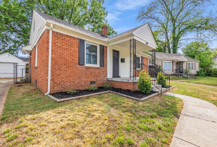 Bungalow-style home with brick siding, a front yard, a chimney, and covered porch