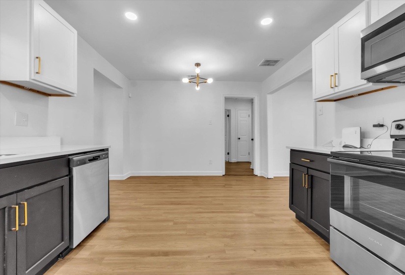 Kitchen featuring stainless steel appliances, hanging lights, light wood-style floors, and white cabinetry
