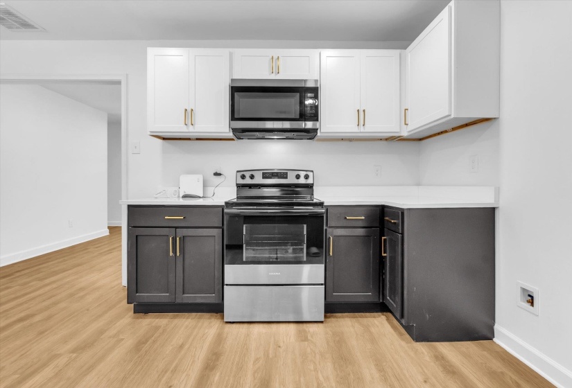 Kitchen featuring dual tone cabinetry, stainless steel appliances, light wood-style flooring, and light stone counters