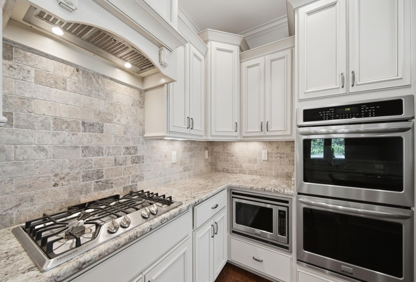 Kitchen with stainless steel appliances, white cabinetry, light stone countertops, and backsplash