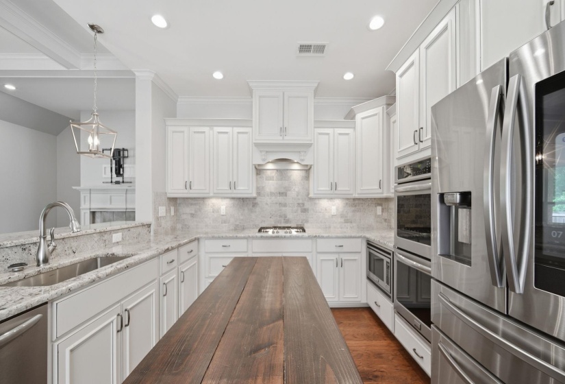 Kitchen with stainless steel appliances, light stone countertops, white cabinetry, ornamental molding, and tasteful backsplash