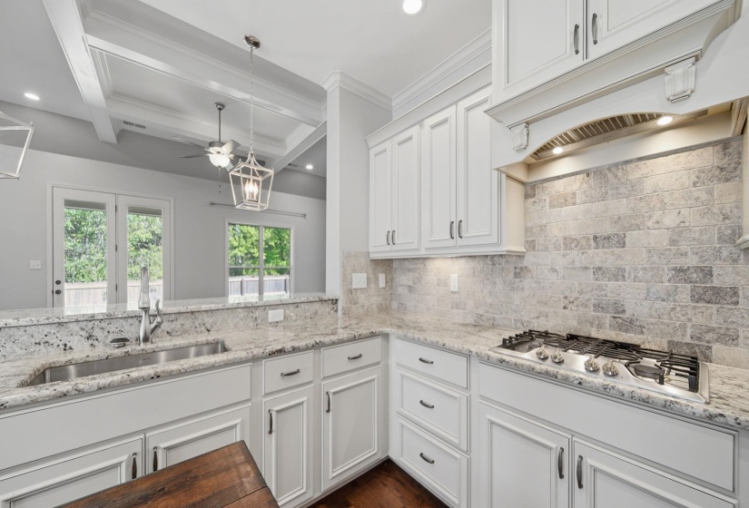 Kitchen featuring white cabinetry, light stone countertops, decorative light fixtures, dark wood-style flooring, and stainless steel gas cooktop