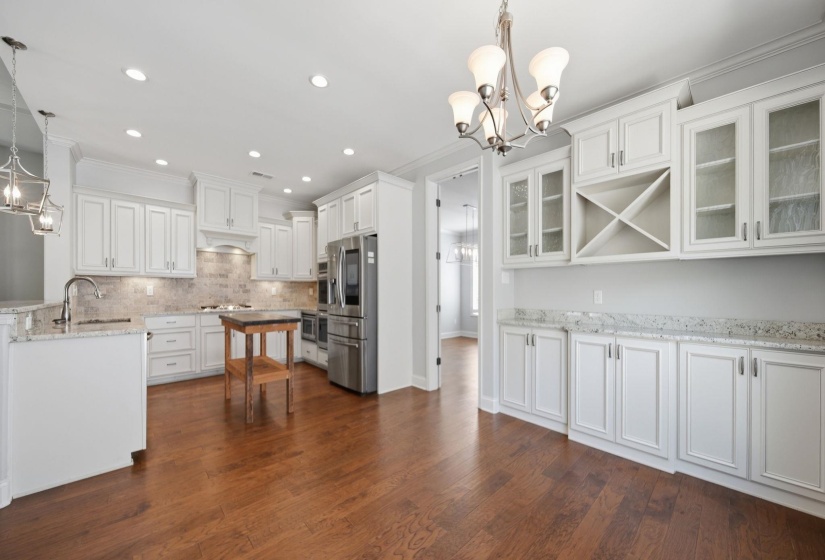 Kitchen featuring hanging lights, white cabinetry, light stone counters, glass fronted cabinets, and dark wood-style floors