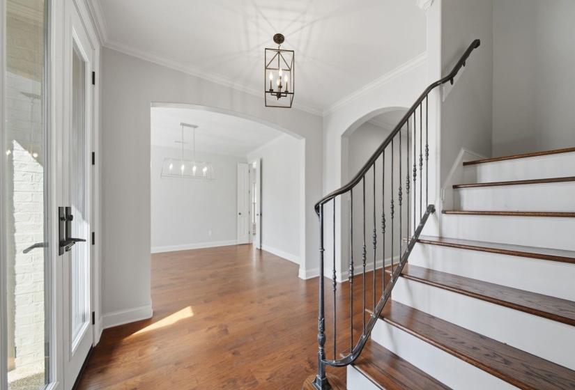 Foyer entrance with a chandelier, dark wood-style flooring, crown molding, and arched walkways
