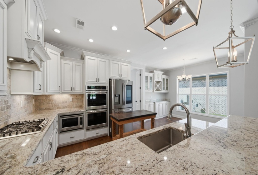 Kitchen with white cabinets, light stone countertops, stainless steel appliances, and ornamental molding