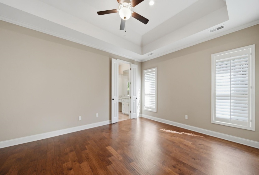 Unfurnished bedroom featuring dark wood-type flooring, connected bathroom, a ceiling fan, a raised ceiling, and crown molding