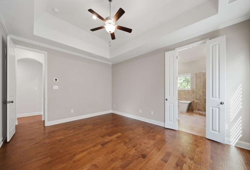 Unfurnished bedroom featuring ornamental molding, arched walkways, dark wood finished floors, a ceiling fan, and connected bathroom