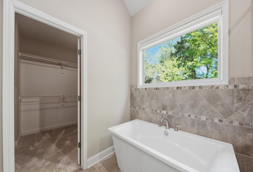 Bathroom with a freestanding bath, a spacious closet, and tile walls