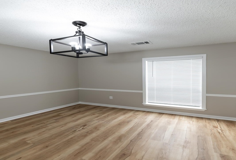 Empty room with suspended lighting, light wood-style flooring, and a textured ceiling