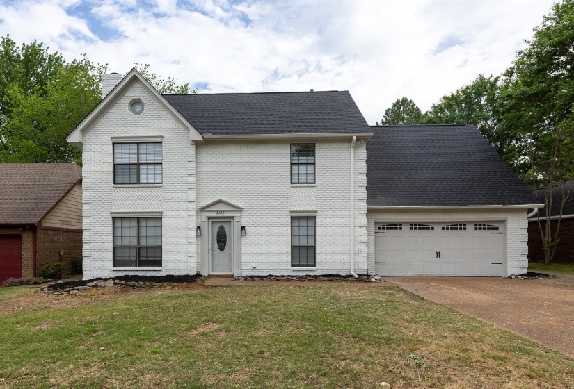 View of front of property featuring a garage, driveway, brick siding, a front lawn, and roof with shingles