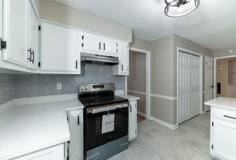 Kitchen featuring stainless steel electric range oven, white cabinetry, tasteful backsplash, and a textured ceiling