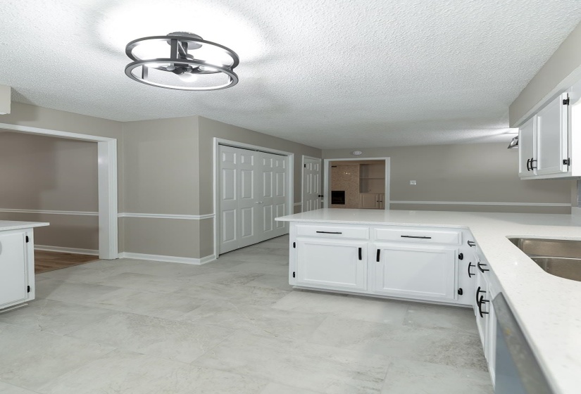 Kitchen featuring white cabinetry, a peninsula, a textured ceiling, light stone counters, and stainless steel dishwasher