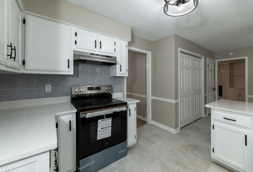 Kitchen with stainless steel electric stove, white cabinets, a textured ceiling, light stone countertops, and tasteful backsplash