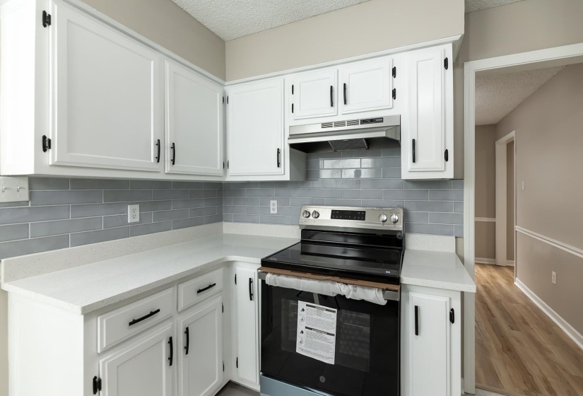 Kitchen with stainless steel electric range, white cabinets, a textured ceiling, light stone countertops, and light wood finished floors